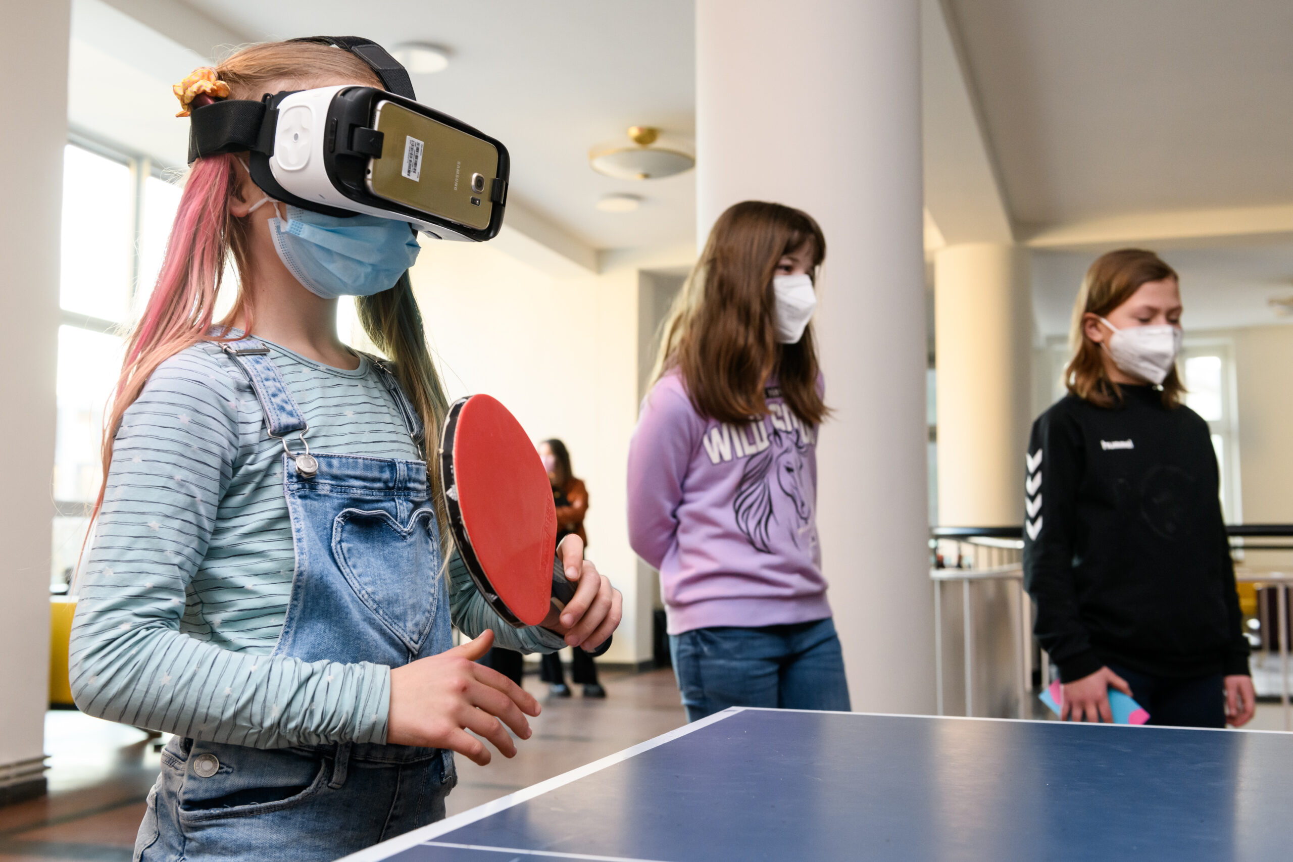 Photograph of a little girl wearing a virtual reality visor while playing table tennis