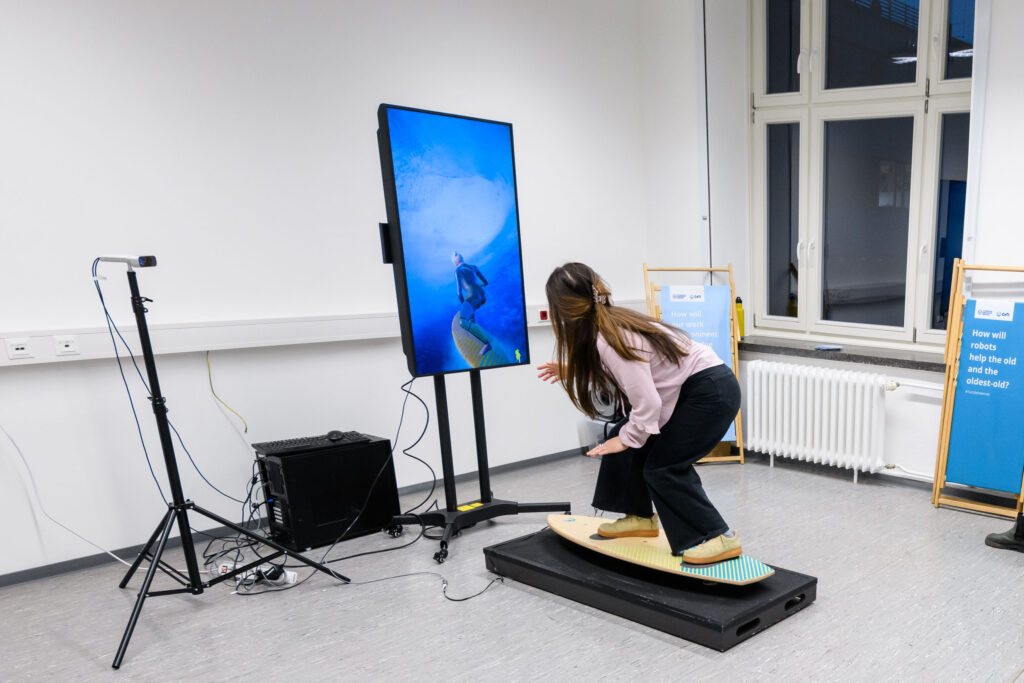 Photograph of a girl on a wooden surfboard in front of a monitor showing the girl's position
