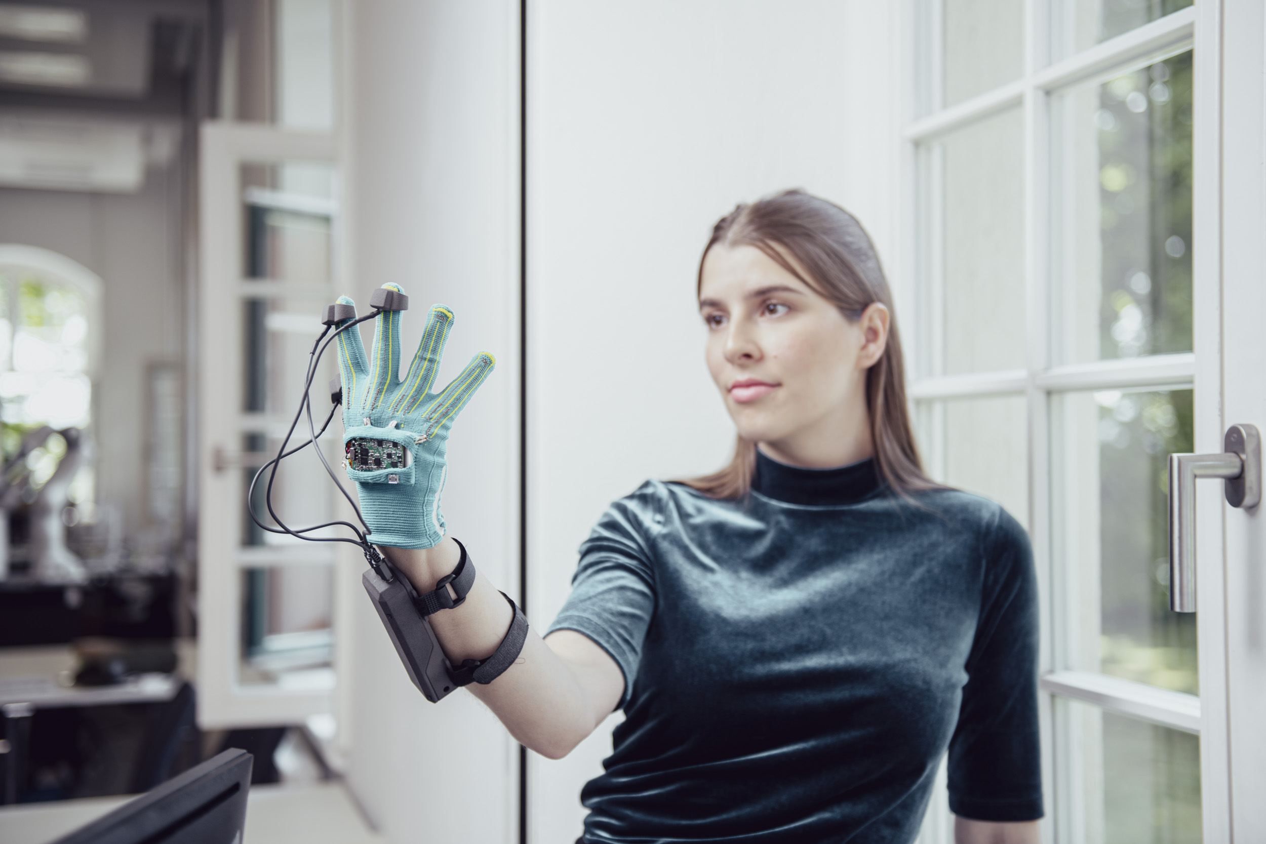 A woman standing next to a window wearing a smart glove with sensors attached to her arm