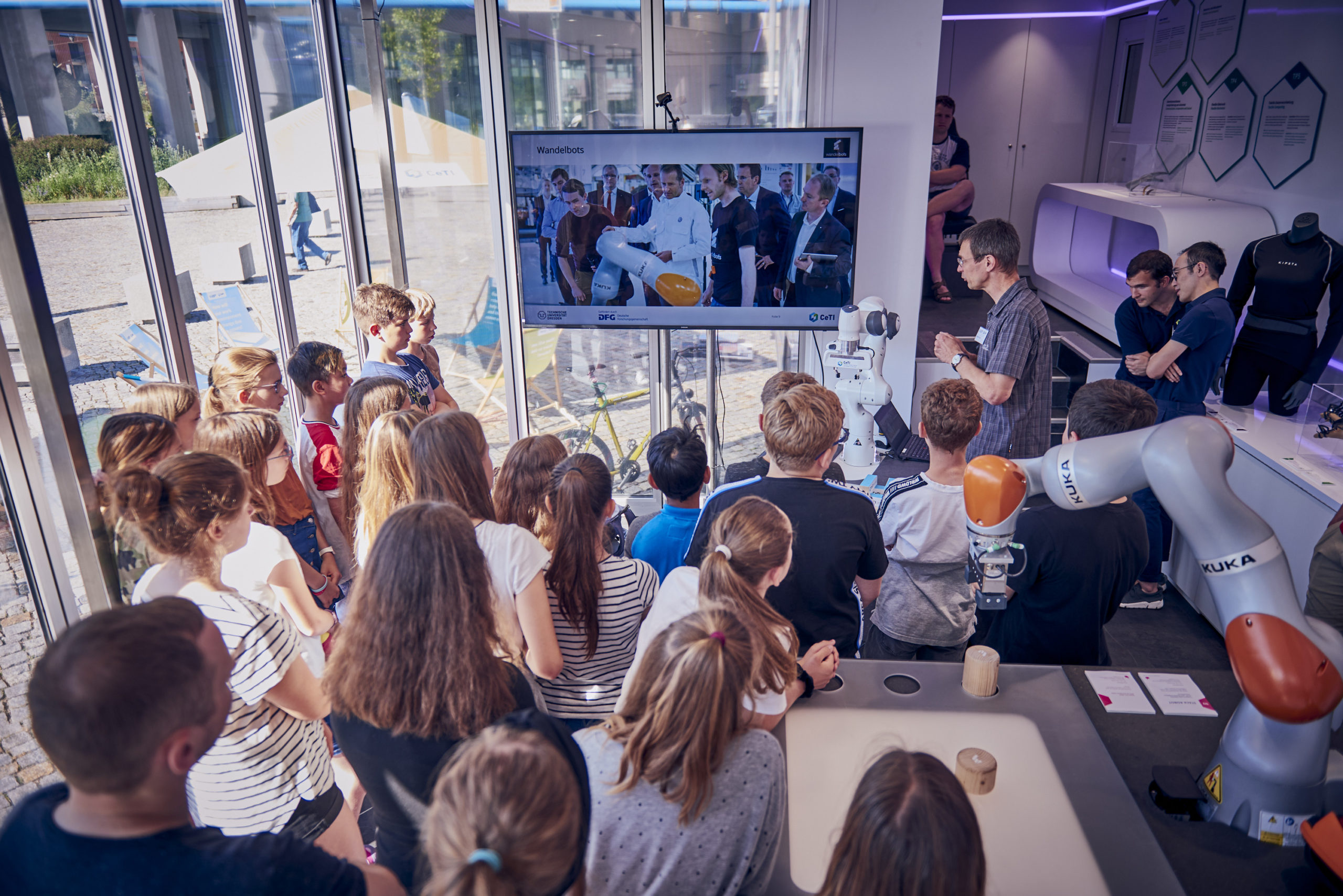 Picture of a group of children listening to a researcher's explanation of robotic arms