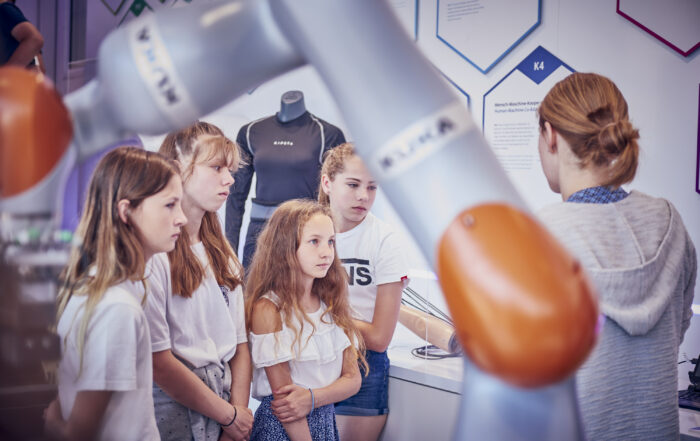 Image of little girls listening to a researcher's explanation of robotics
