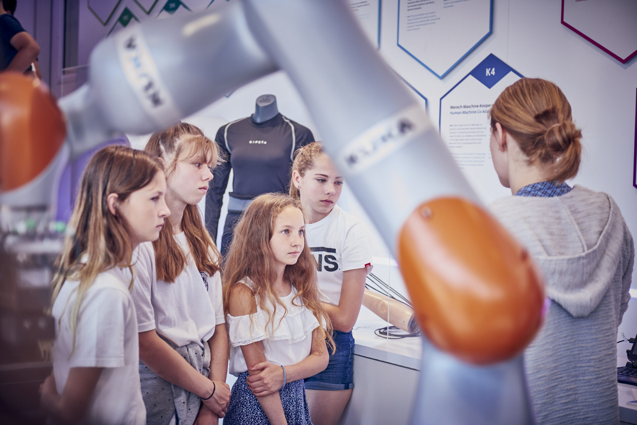 Image of little girls listening to a researcher's explanation of robotics