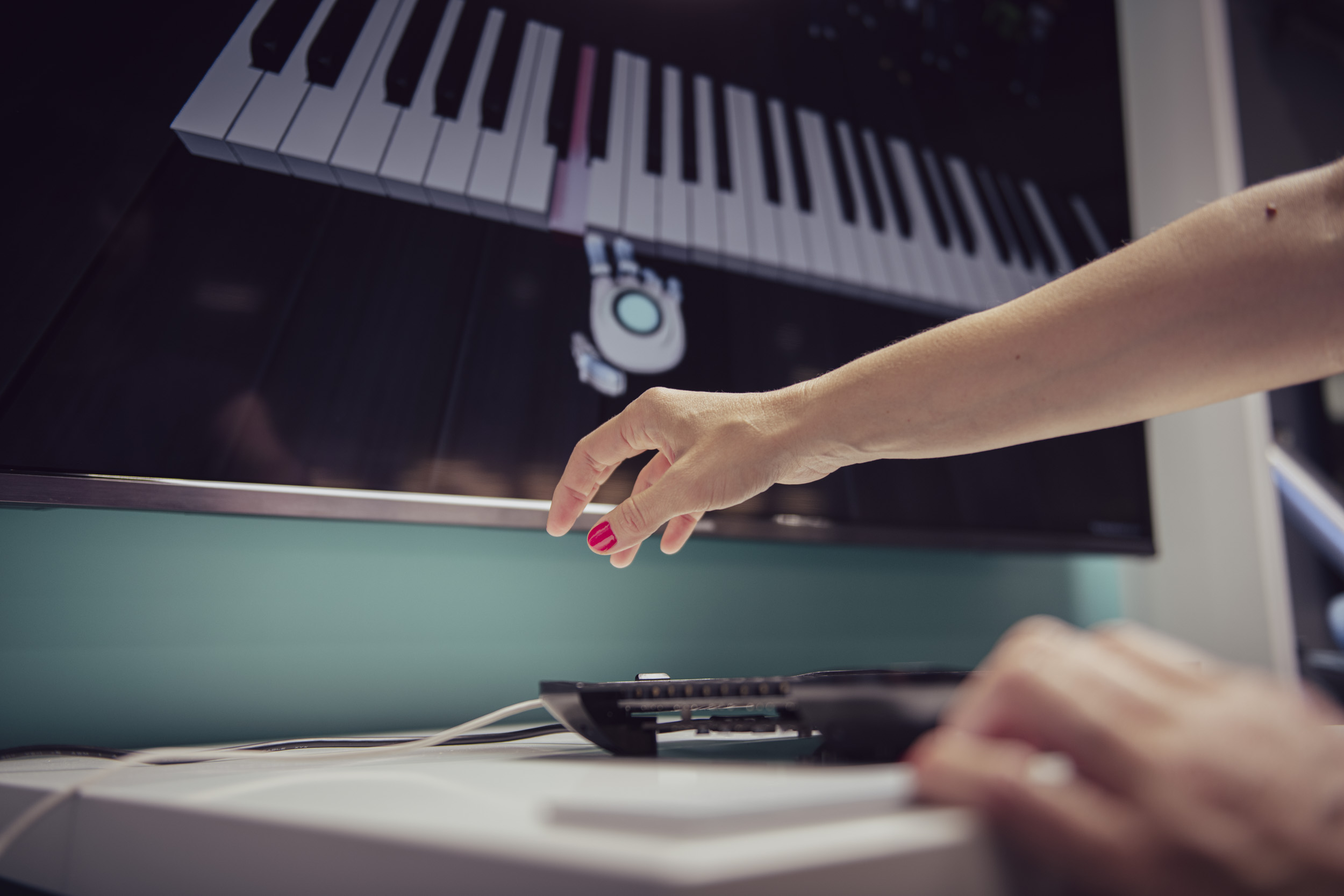 Eine ausgestreckte Hand mit rot lackierten Nägeln und einem Bildschirm, auf dem virtuell ein Klavier gespielt wird