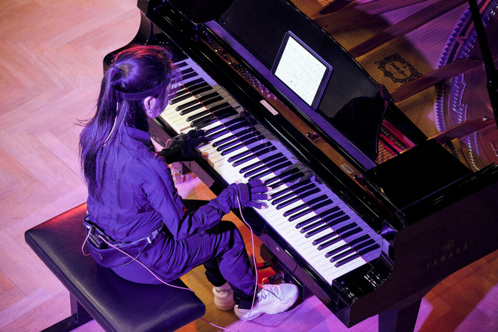 A person playing a grand piano while being connected to a haptic force-feedback system