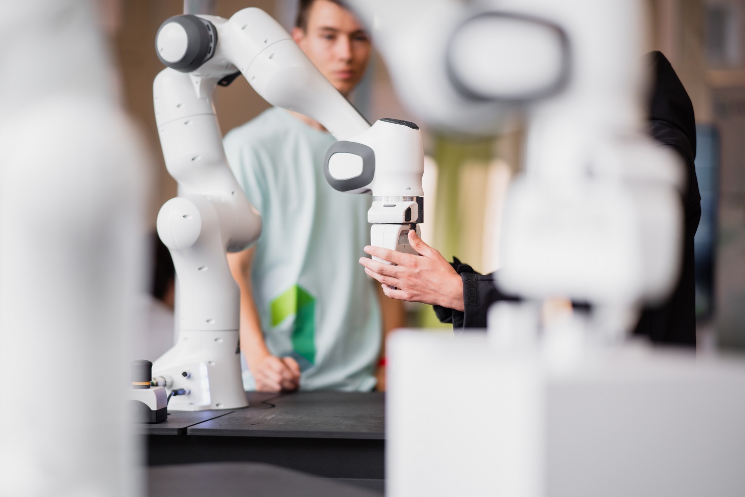 Two people standing around a robotic arm observing it