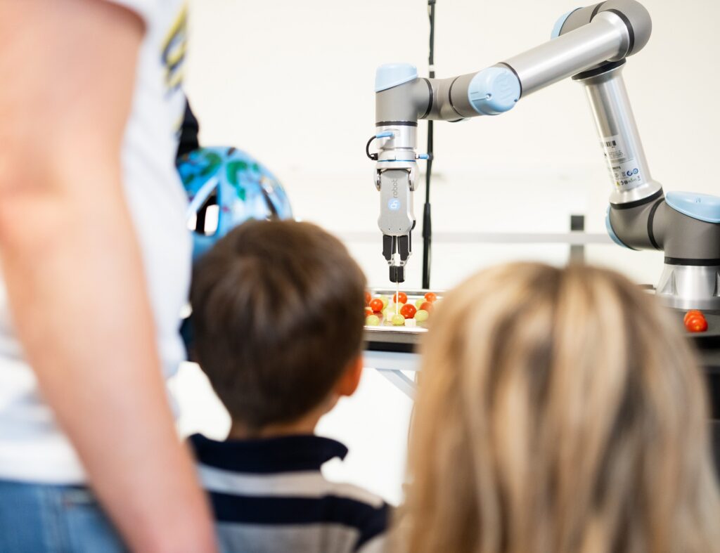 A robotic arm picking up a grape while children watching it