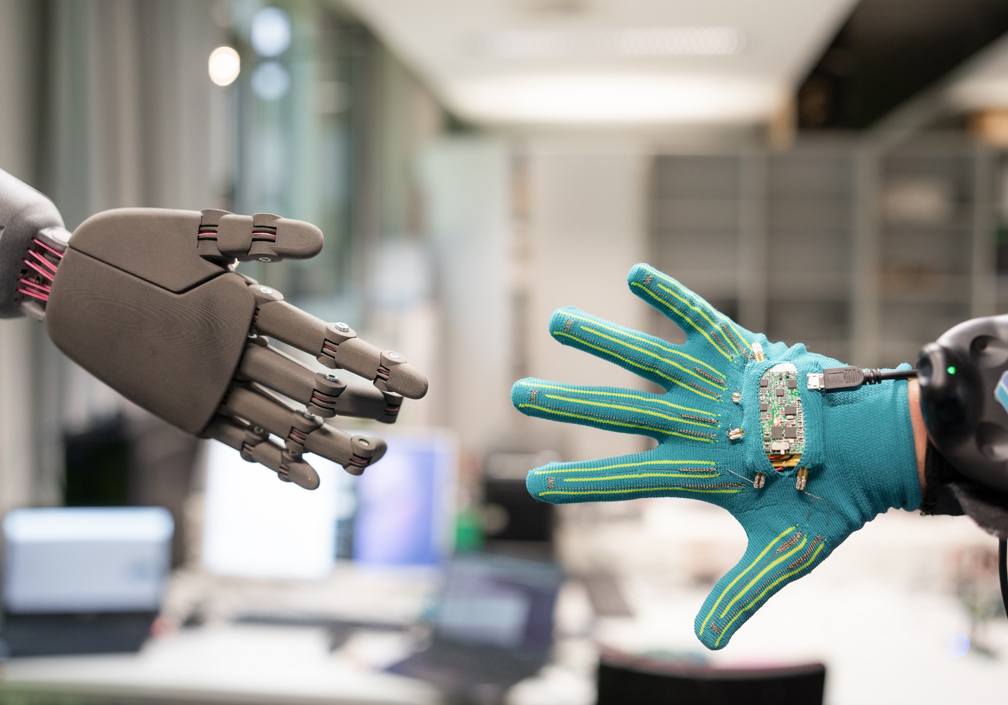 A robotic hand and a human hand wearing the Fingertac Demonstrator reaching towards each other