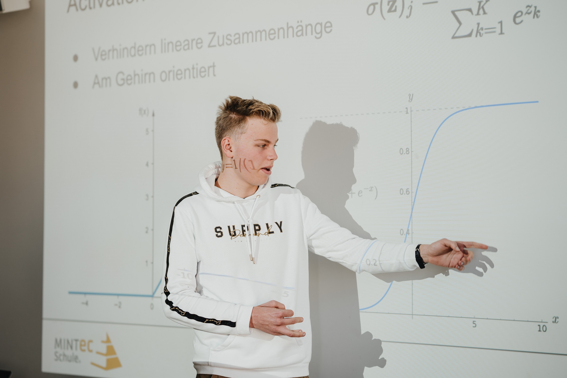 Photograph of a boy pointing towards a graph on a presentation slide that is projected against a wall