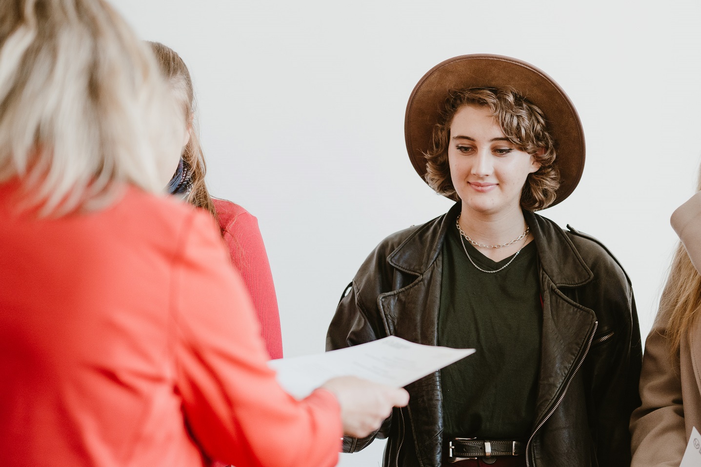 Photograph of a girl wearing a hat receiving a paper from a person