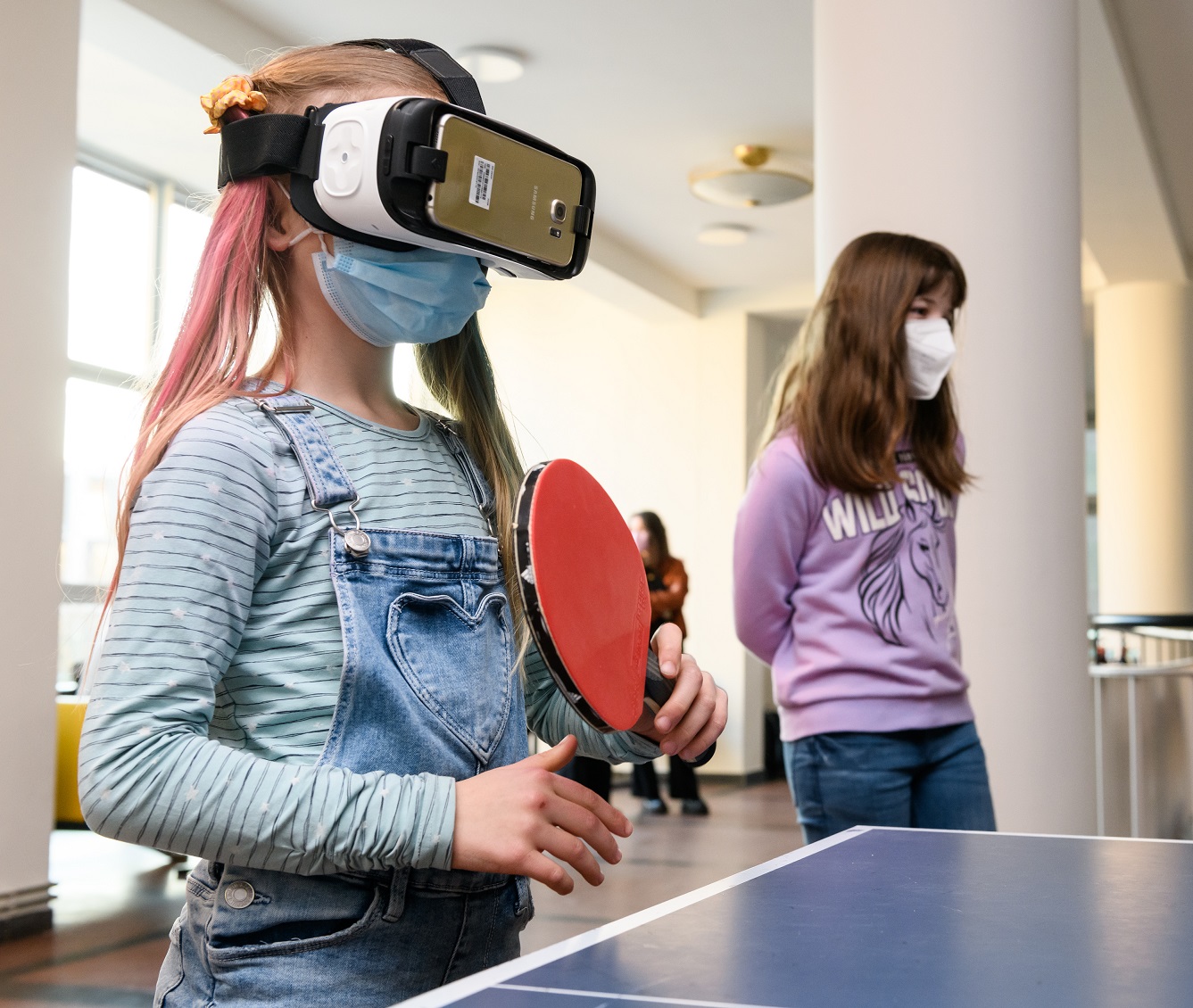 Photograph of a little girl wearing a virtual reality visor while playing table tennis