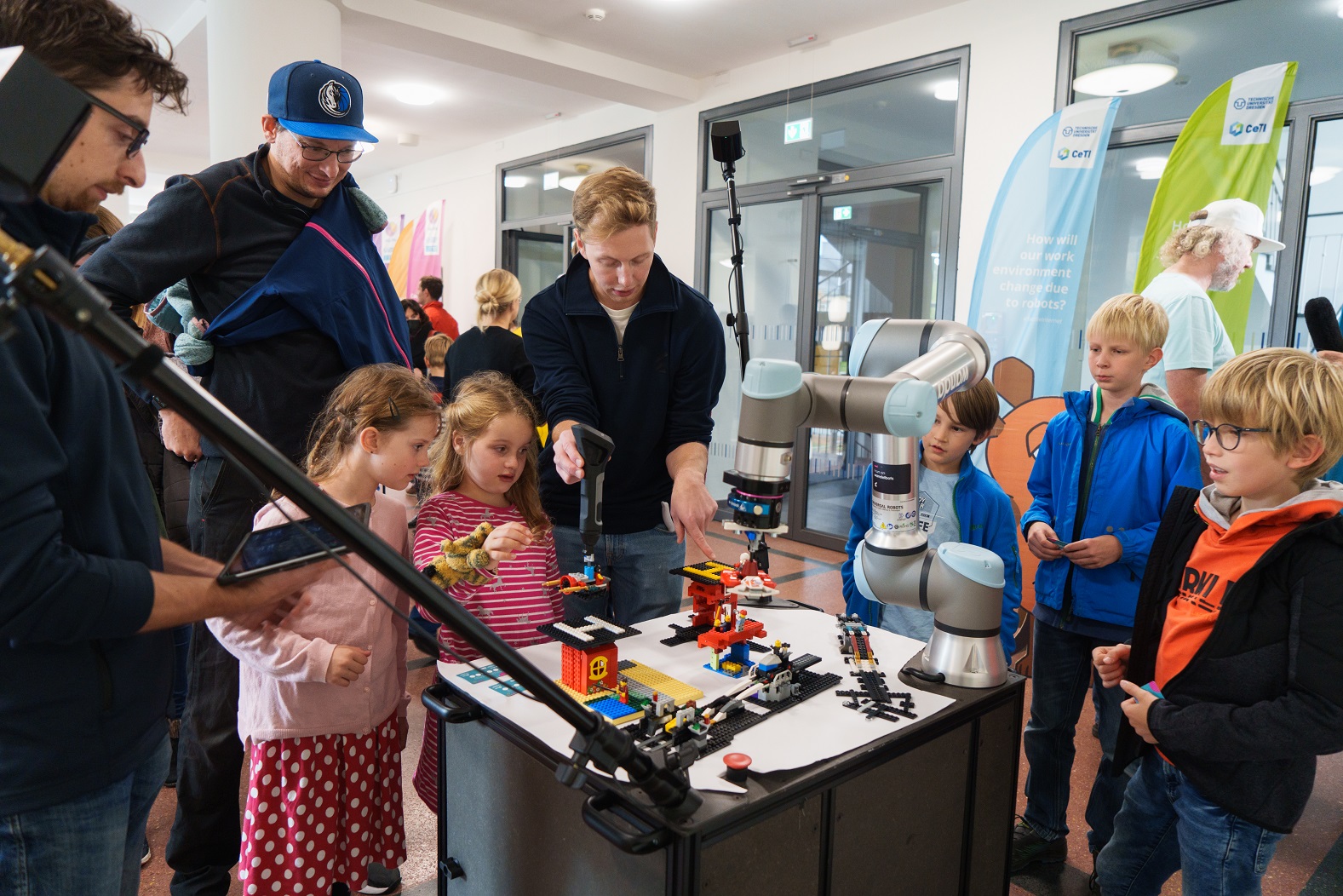 Photograph of a group of boys and girls around a robotic demonstrator while a researcher explains how it works