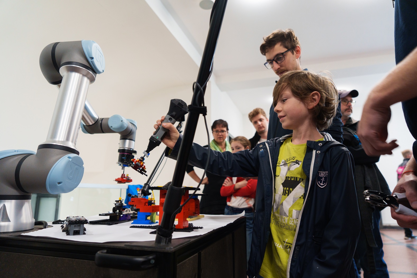 Photograph of a child testing a robotic demonstrator. The demonstrator consists of a robotic arm, a robotic pen and Lego models.