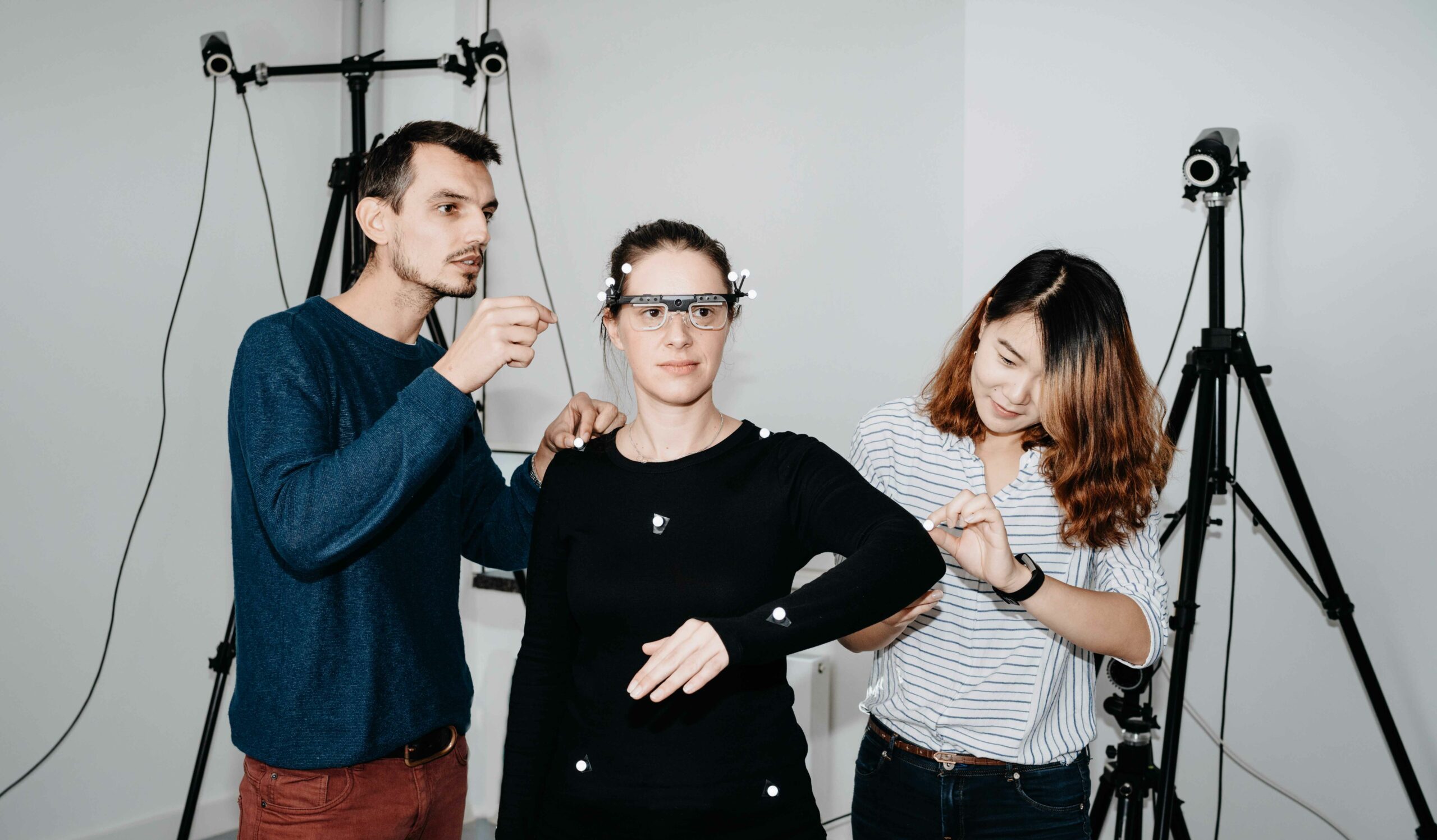 A woman wearing an IMUmotion capture suit with two people around her helping with the suit