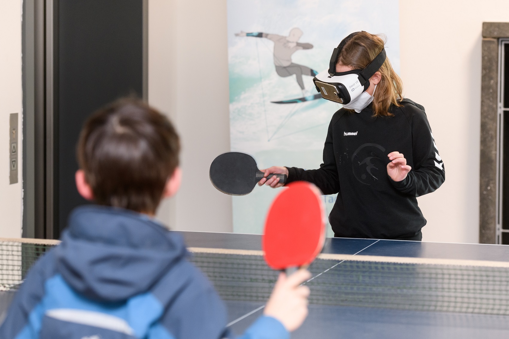 Photograph of a girl wearing a virtual reality visor while playing table tennis with another child